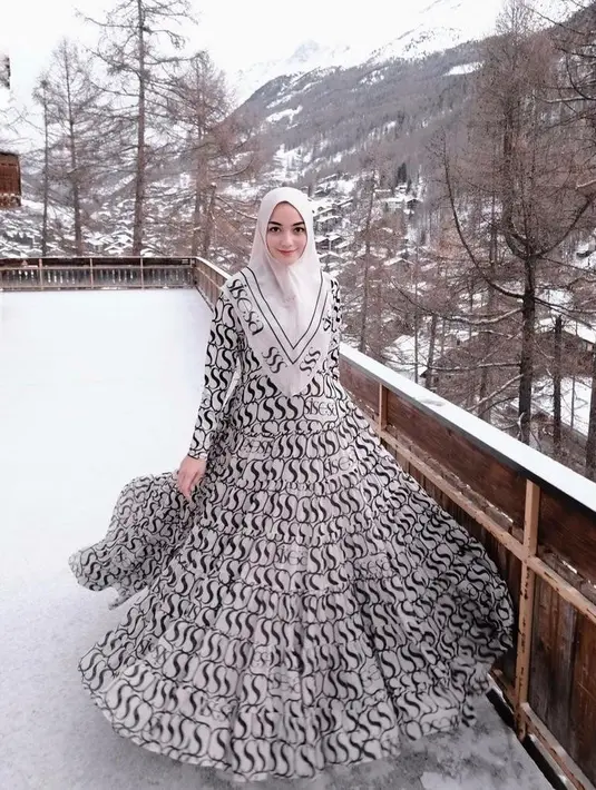 Berpose di hamparan salju Swiss, istri Rezky Aditya ini tampak anggun berbalut dress dan hijab monokrom.