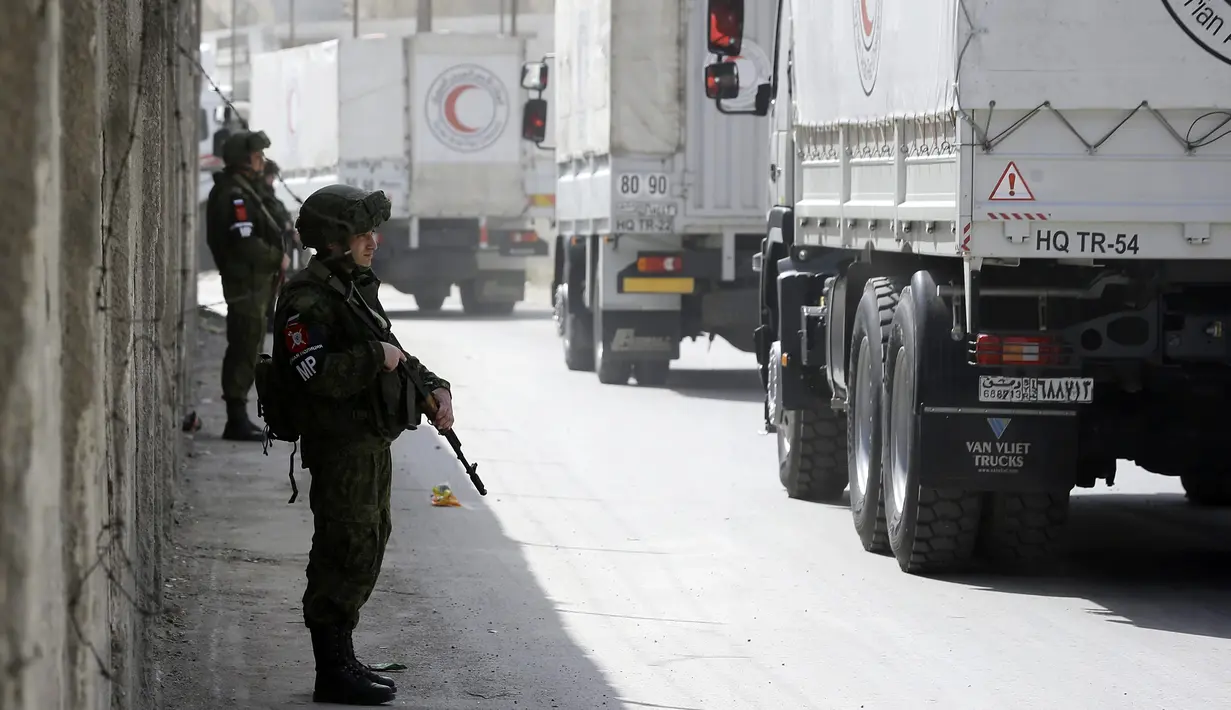 Tentara Rusia berjaga-jaga saat konvoi truk bantuan melewati pos pemeriksaan Al-Wafideen, Damaskus, Suriah, Senin (5/3). Konvoi tersebut untuk memberikan bantuan bagi warga Ghouta Timur. (AFP PHOTO/LOUAI BESHARA)