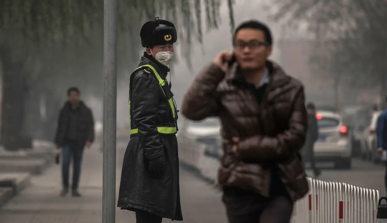 Petugas mengenakan masker saat kabut asap menyelimuti Beijing, China, Senin (30/11). Pemerintah setempat mengumumkan keadaan siaga dan menyarankan warga Beijing untuk berada dalam rumah karena kandungan polusi udara yang berbahaya. (AFP PHOTO/FRED DUFOUR)