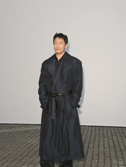 Son Suk-ku tampil dengan trench coat navy panjang yang dililit sabuk kulit lebar di pinggang, dipadukan kemeja dan celana serba hitam [dok. Burberry]