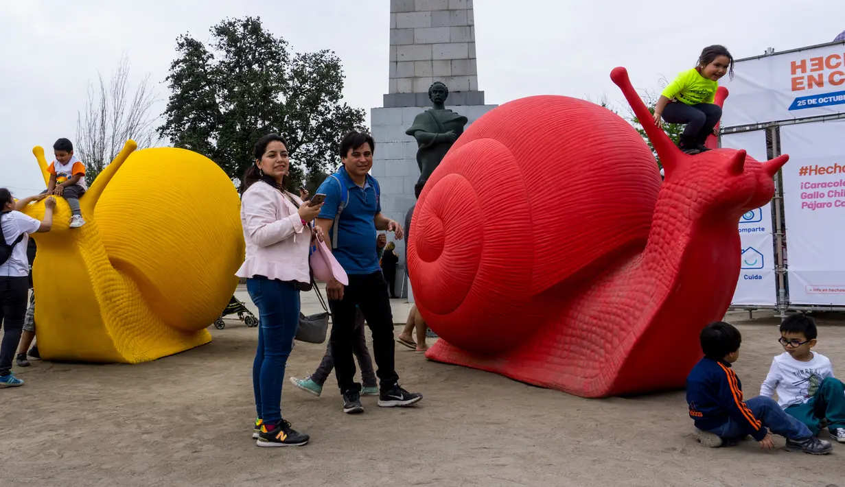 Anak-anak bermain dengan siput raksasa, bagian dari seni instalasi "Hecho en Casa" yang menghiasi pedestrian kota Santiago, Chile, Senin (29/10). Siput raksasa dari plastik daur ulang itu dibuat oleh Cracking Art Group asal Italia. (Martin BERNETTI/AFP)