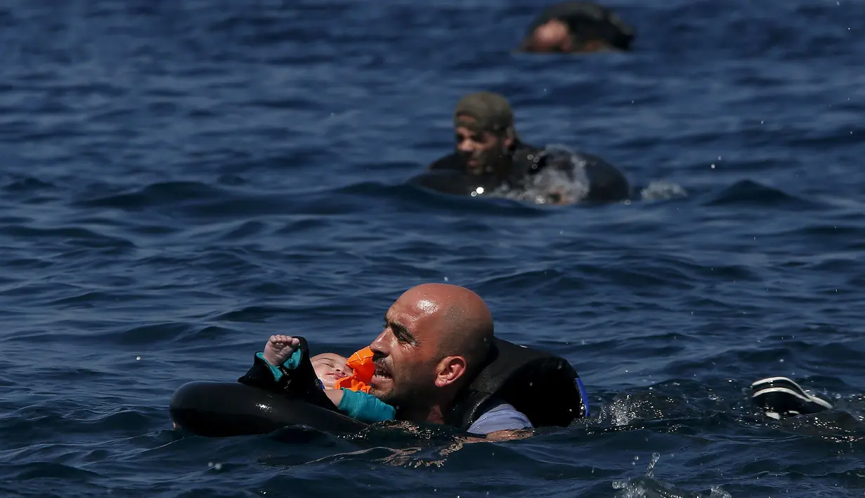 Seorang pengungsi Suriah membawa bayi menggunakan pelampung dan berenang menuju pantai setelah perahu yang ditumpangi bocor sekitar 100 m sebelum mencapai pulau Lesbon, Yunani, Minggu (13/09/2015). (REUTERS/Alkis Konstantinidis) 