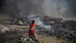 Seorang wanita berjalan tanpa alas kaki di dekat gubuk yang terbakar di daerah kumuh di Noida, pinggiran kota New Delhi, India, Minggu (11/4/2021). Dua anak tewas dan lebih dari 150 gubuk kumuh yang sebagian besar dihuni oleh para pemulung dalam kebakaran pada Minggu sore. (AP Photo/Altaf Qadri)