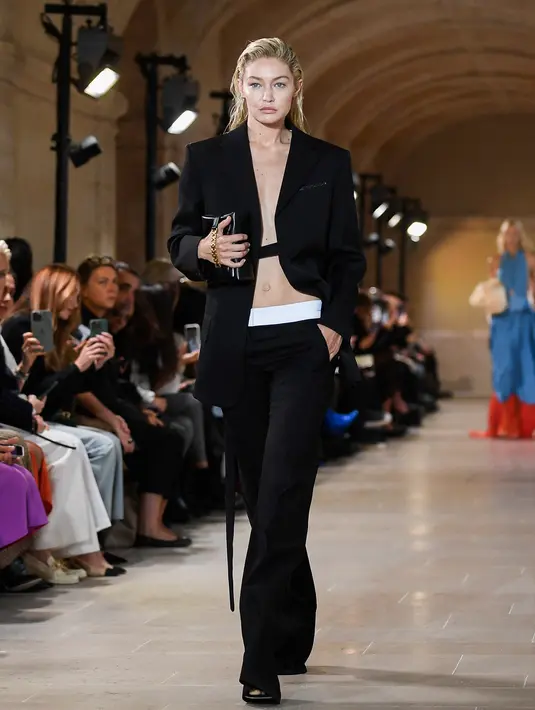 <p>Model AS Gigi Hadid mempersembahkan kreasi untuk peragaan busana Victoria Beckham Spring-Summer 2023 pada Paris Womenswear Fashion Week di Paris, Prancis, 30 September 2022. Penampilan Gigi kian menawan dilengkapi sepasang celana panjang hitam dengan ikat pinggang putih tebal serta tali yang digantung pada jaket bergaya. (JULIEN DE ROSA/AFP)</p>