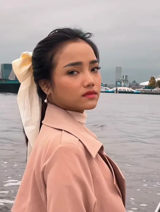 Kali ini, Fuji  tampil lebih feminim mengenakan turtleneck, rok plisket putih, dan  long coat warna khaki. Penampilannya makin manis dengan kunciran pita. [@fuji_an]