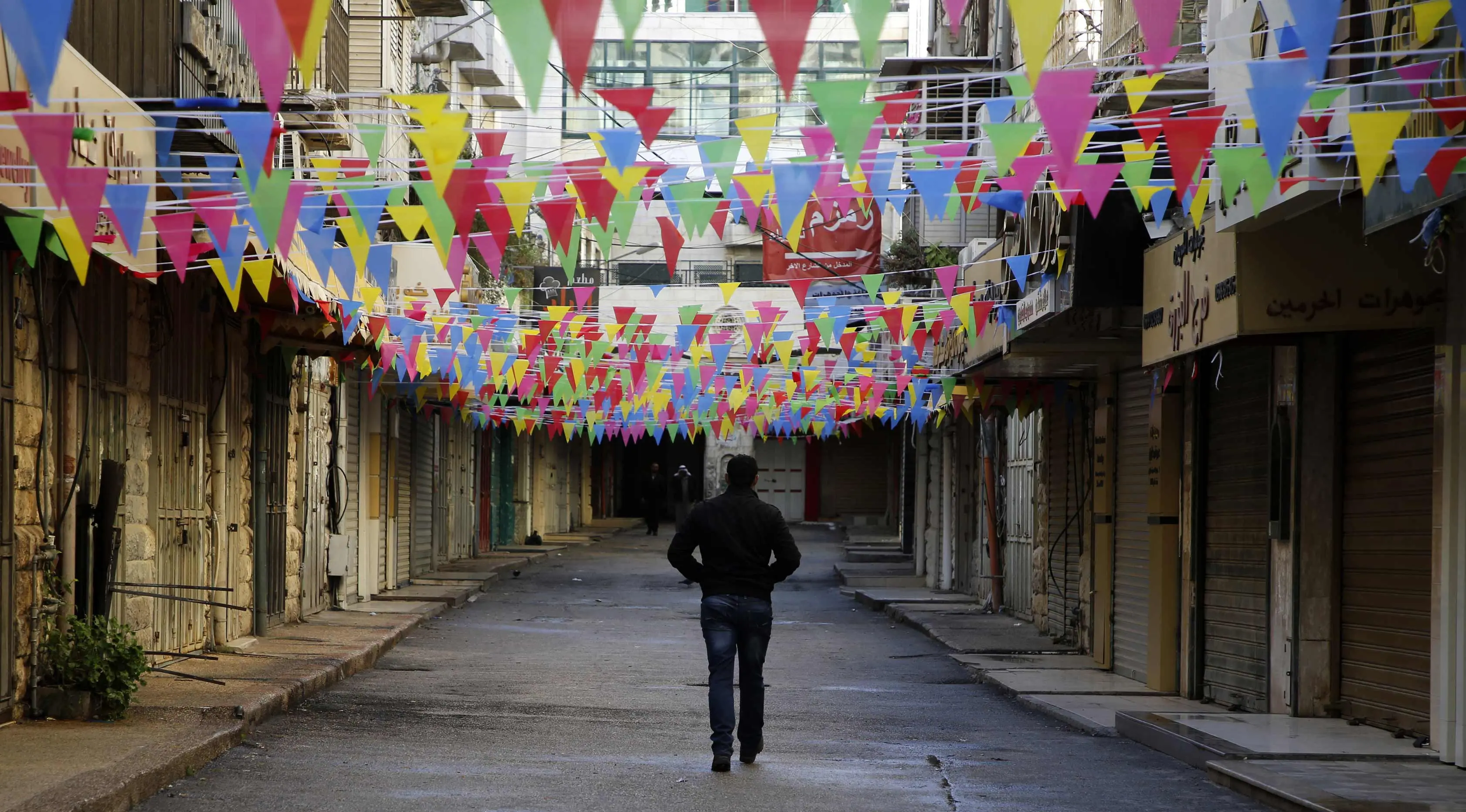 Seorang pria Palestina berjalan melewati toko-toko yang tutup di kota Nablus, Tepi Barat, (7/12). Usai Presiden AS, Donald Trump mengumumkan Yerusalem sebagai ibu kota Israel suasana sepi terlihat di kawasan tersebut. (AFP Photo/Jaafar Ashtiyeh)