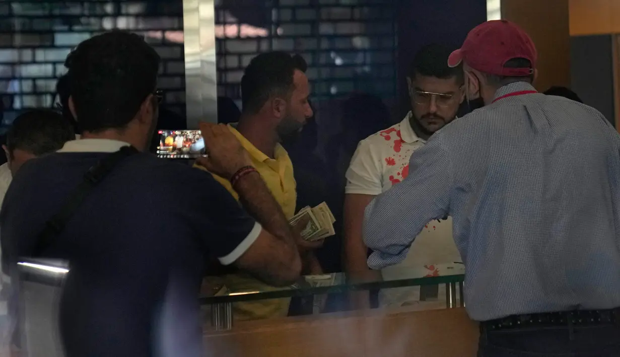 Seorang nasabah yang menabung di cabang Bank BLOM (tengah) yang menyerang bank dengan seorang wanita bersenjata dan belasan aktivis, menerima dolar AS, Beirut, Lebanon, Rabu (14/9/2022). Saat aksi pembobolan terjadi Hafez mengangkat pistol mainannya dan mengambil $ 13.000 dari rekening tabungannya yang terperangkap. (AP Photo/Hussein Malla)