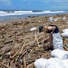 Seorang turis asing mengumpulkan sampah di antara tumpukan puing di pantai di Batu Belig di Kabupaten Badung setelah hanyut menyusul badai lepas pantai di Bali (14/12/2021). (AFP/Sony Tumbelaka)