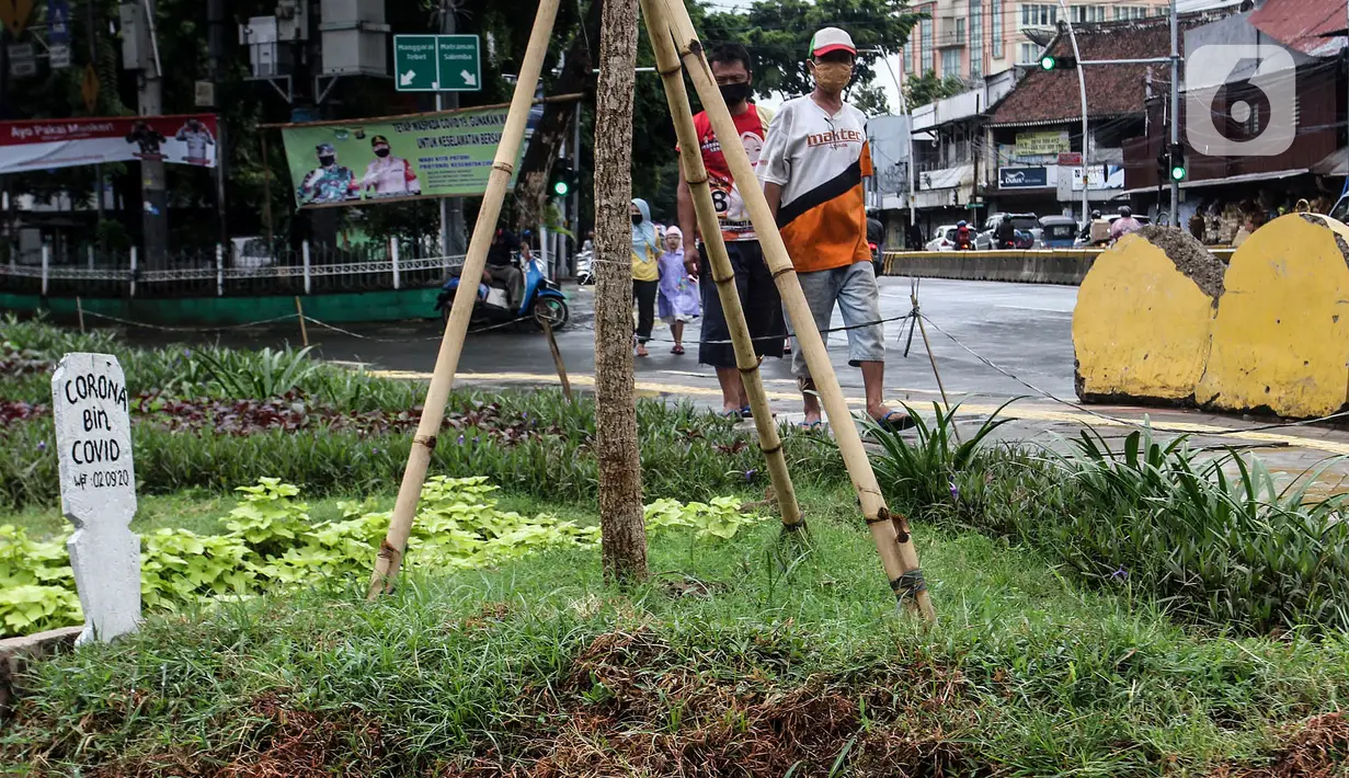 Warga melihat kuburan dengan papan nisan bertuliskan Corona bin Covid di taman Jalan Jatinegara Barat, Jakarta, Minggu (20/9/2020). Kuburan tersebut sengaja dibuat untuk mengingatkan masyarakat yang melintas akan bahaya virus Covid-19. (Liputan6.comm/Johan Tallo)