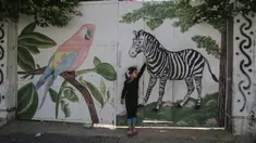 Seorang gadis Palestina menyentuh mural zebra di luar kebun binatang lokal yang ditutup di Rafah di Jalur Gaza selatan (26/5/2020). Kebun binatang itu ditutup selama liburan Idul Fitri karena pandemi virus coronavirus COVID-19. (AFP/Said Khatib)