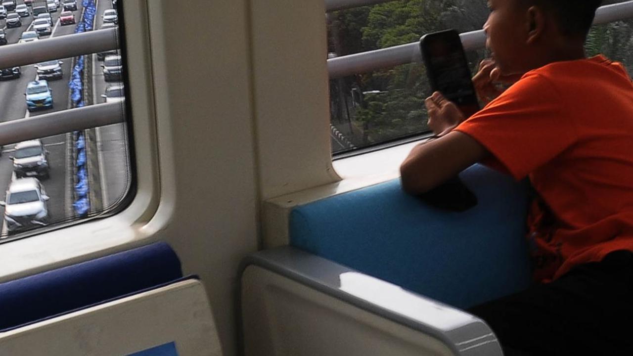 Seorang penumpang anak tampak menikmati perjalanan dengan LRT Jabodebek sambil memotret pemandangan ibu kota dengan kamera ponselnya.