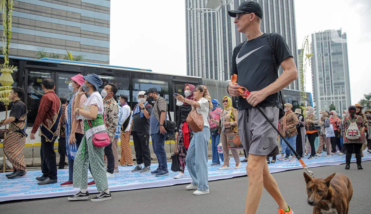 Warga berolahraga saat sejumlah orang yang mengenakan batik berjalan di catwalk sepanjang Jalan Jenderal Sudirman, Jakarta, Minggu (2/10/2022). Kegiatan yang diikuti ratusan orang ini diselenggarakan oleh Bank Mandiri untuk menyambut Hari Batik Nasional yang jatuh setiap tanggal 2 Oktober 2022. (Liputan6.com/Faizal Fanani)