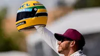 Pebalap Mercedes, Lewis Hamilton, memegang helm Ayrton Senna yang merupakan hadiah dari pihak keluarga driver asal Brasil itu. Helm itu diberikan setelah kualifikasi F1 GP Kanada, Sabtu (10/6/2017). (EPA/VALDRIN XHEMAJ)