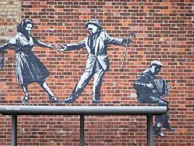 Sebuah karya seni grafiti dari pasangan yang menari dengan pemain akordeon, yang menyandang ciri khas seniman jalanan Banksy, terlihat di dinding di Great Yarmouth di pantai timur Inggris pada 8 Agustus 2021. Karya tersebut belum diklaim oleh Banksy. (JUSTIN TALLIS / AFP)