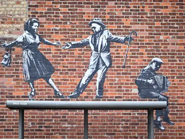 Sebuah karya seni grafiti dari pasangan yang menari dengan pemain akordeon, yang menyandang ciri khas seniman jalanan Banksy, terlihat di dinding di Great Yarmouth di pantai timur Inggris pada 8 Agustus 2021. Karya tersebut belum diklaim oleh Banksy. (JUSTIN TALLIS / AFP)