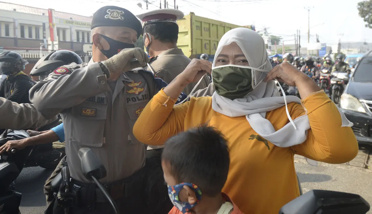 Anggota polisi dari Polsek Parung membantu memasangkan masker kepada pengendara sepeda motor di depan Polsek Parung, Kabupaten Bogor, Jawa Barat, Rabu (2/9/2020). Pembagian masker gratis ini untuk mengajak masyarakat hidup sehat dan mencegah penular COVID-19. (merdeka.com/Dwi Narwoko)