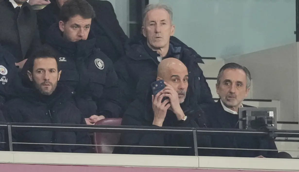 Pelatih Manchester City, Pep Guardiola, memberikan arahan melalui telpon dari tribun penonton saat anak asuhnya bermain imbang 1-1 melawan West Ham United pada pekan ke-30 Premier League 2025/2026 di London Stadium pada Minggu (15/3/2026). (AP Photo/Dave Shopland)