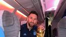 Kapten dan penyerang Argentina Lionel Messi duduk sambil berpose dengan Trofi Piala Dunia 2022 saat berada di dalam pesawat. Trofi Piala Dunia 2022 melengkapi gelar yang direbut Messi bersama klub, negara, dan individu. (Instagram/leomessi)