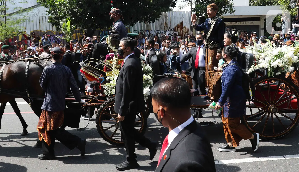 Presiden Joko Widodo menyapa warga saat menaiki kereta dalam mengikuti prosesi kirab Ngunduh Mantu di kawasan Selamet Riyadi, Solo, Jawa Tengah, Minggu (11/12/2022). Kirab ngunduh mantu pernikahan putra bungsu Presiden Joko Widodo, Kaesang Pangarep dan istrinya Erina Gudono yang dimulai dari Loji Gandrung menuju Pura Mangkunegaran tersebut disaksikan ribuan masyarakat Solo dan sekitarnya. (Liputan6.com/Herman Zakharia)