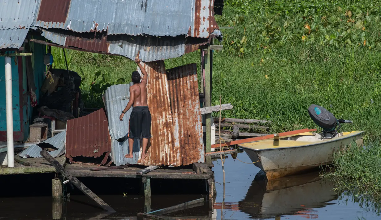 Seorang pria memperbaiki atap rumah panggungnya di Congo Mirador, negara bagian Zulia, Venezuela, pada 6 September 2021. Kehidupan indah di Congo Mirador, sebuah desa rumah panggung yang tampak mengapung di perairan laguna di Zulia (barat), tenggelam dalam lumpur dan gulma. (Federico PARRA/AFP)