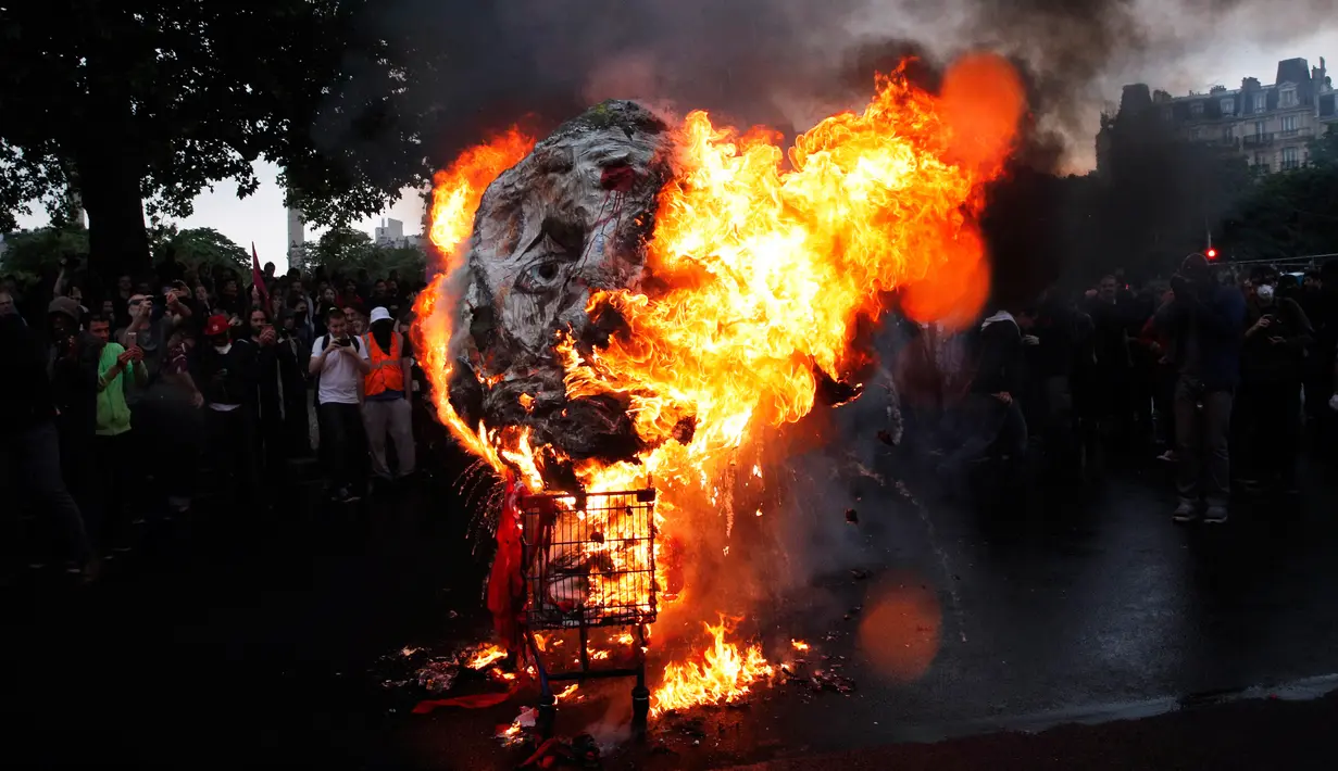 Sebuah topeng raksasa yang menggambarkan Presiden Prancis Emmanuel Macron dibakar selama terjadi demonstrasi di Paris, Prancis (23/5). (AP/Christophe Ena)