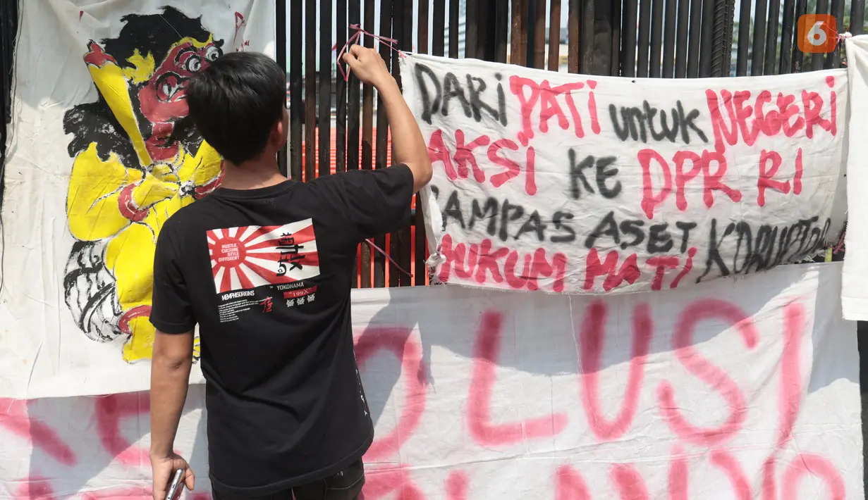 Seorang pengunjuk rasa memasang spanduk berisi tuntutan di pagar gedung DPR saat mengikuti aksi Aliansi Masyarakat Pati Bersatu (AMPB) di Jakarta, Kamis (27/8/2026). (KLY/Budy Santoso)