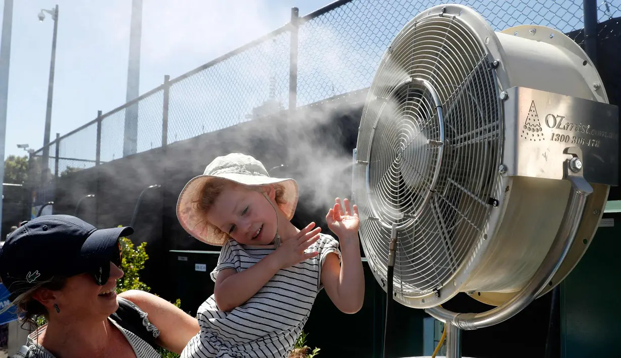 Seorang anak berada di depan kipas pendingin saat menyaksikan pertandingan turnamen tenis Australia Terbuka 2018 di Melbourne, Australia, (16/1). Teriknya matahari membuat peserta dan penonton kepanasan. (AP Photo / Ng Han Guan)
