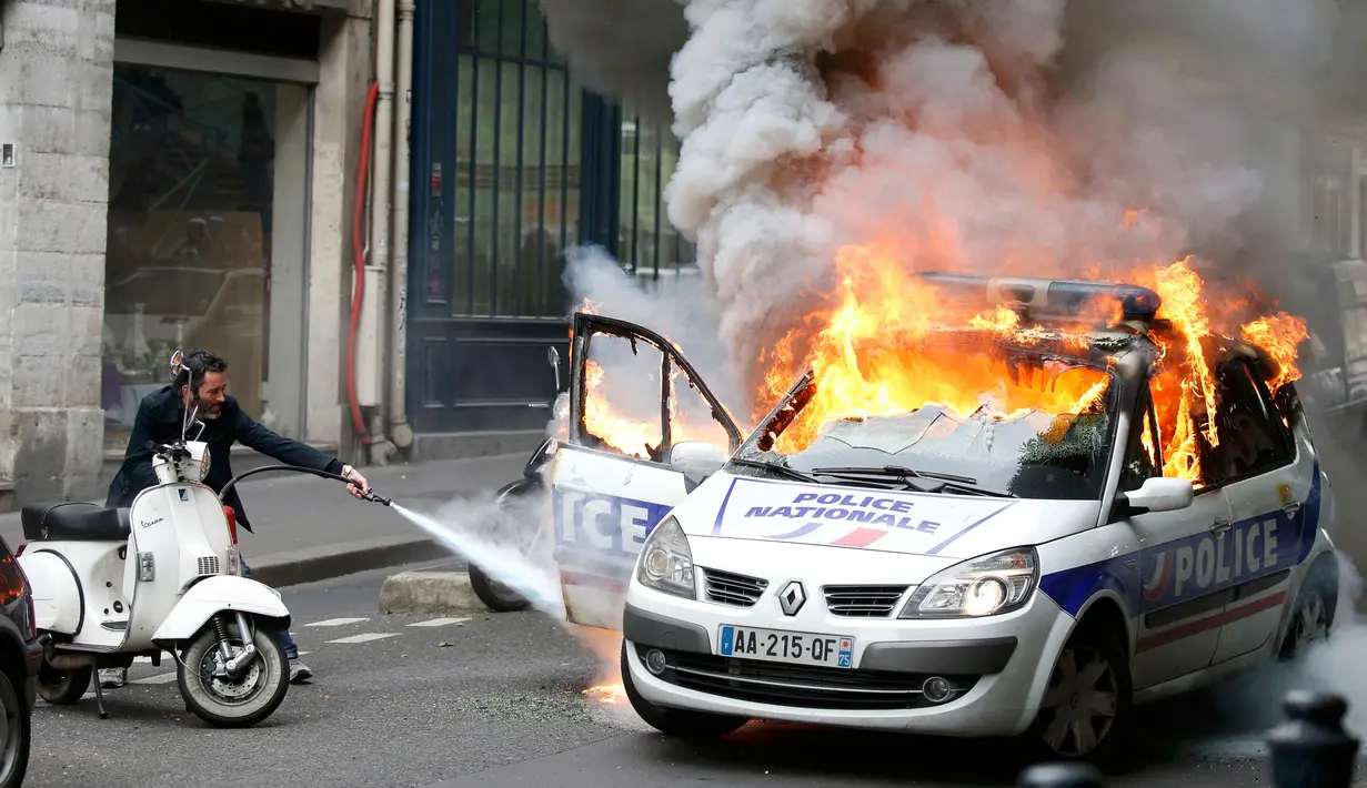 Petugas berusaha memadamkan mobil polisi yang terbakar akibat demo di Paris, Prancis (18/5). Demo buruh tersebut menentang kekerasan polisi dan melawan reformasi hukum yang berakhir bentrok dengan polisi. (REUTERS / Charles Platiau)