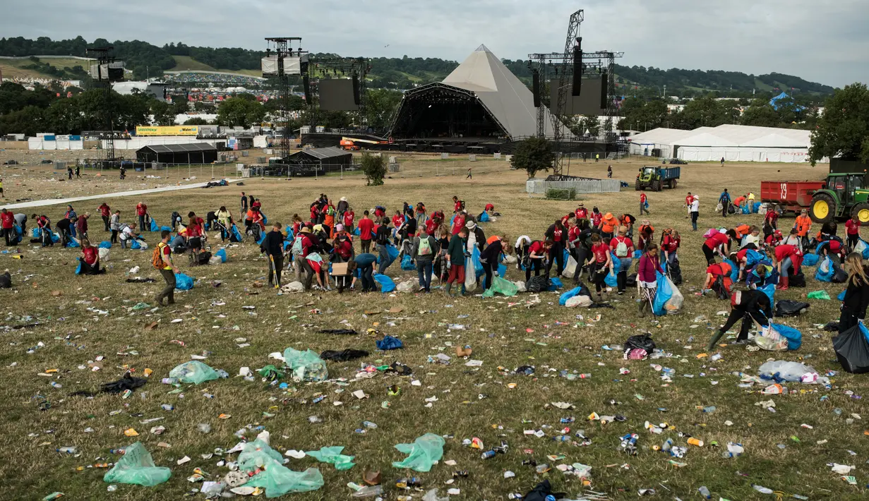 Petugas memungut sampah di depan Pyramid Stage pada akhir Festival Glastonbury di arena Worthy Farm, Inggris, 26 Juni 2017. Penyelenggaraan festival musik terbesar di dunia itu menyisakan sampah yang berserakan di seluruh arena. (OLI SCARFF/AFP)