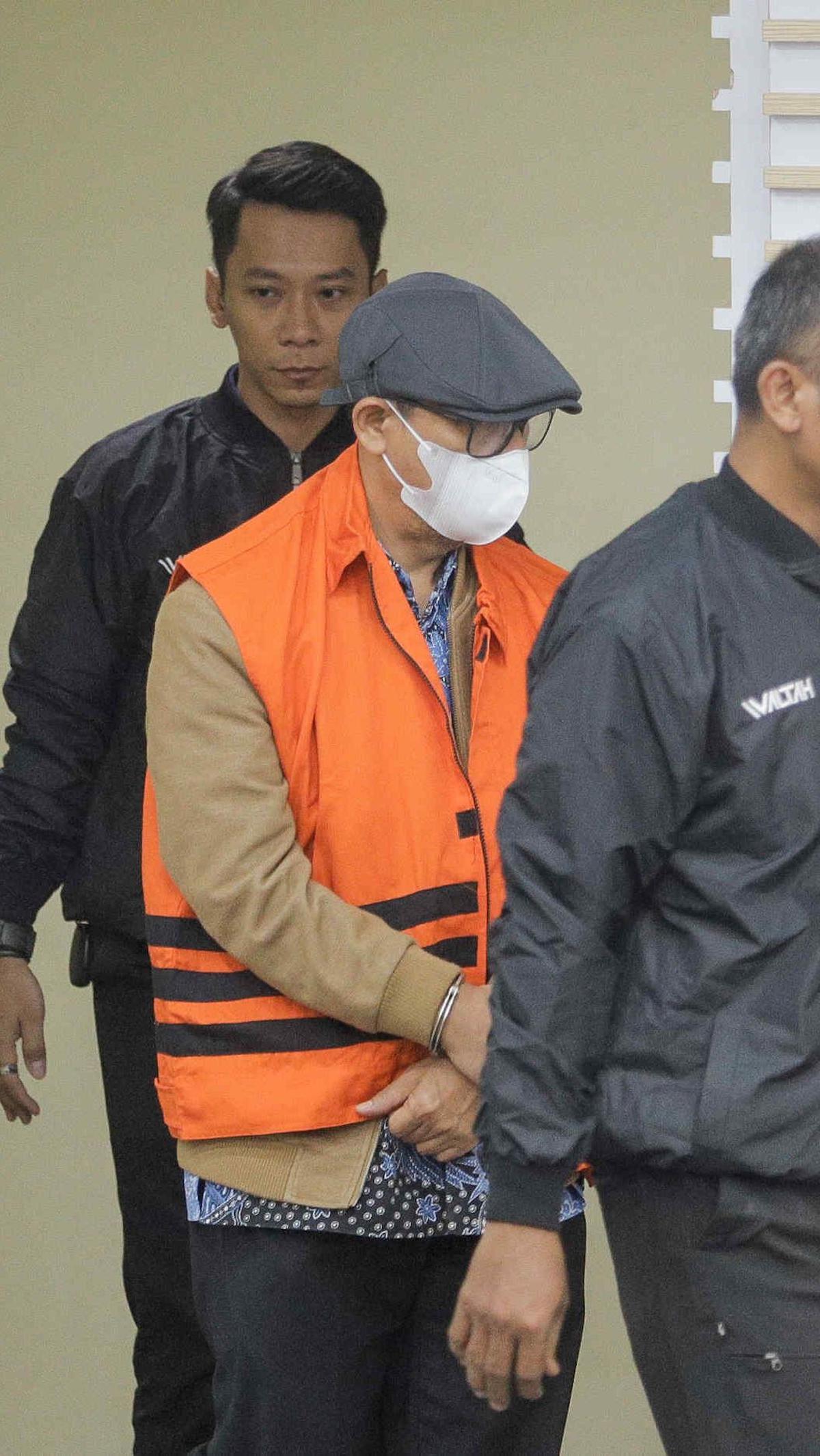 Dia tampak mengenakan rompi oranye KPK dengan tangan diborgol. Sementara, kepalanya lebih banyak menunduk.