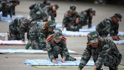 Mahasiswa baru belajar melipat selimut selama sesi pelatihan militer di sebuah kampus di Yangzhou, Jiangsu, China, Jumat (6/9/2019). Rangkaian ospek mahasiswa baru di China umumnya tidak melibatkan senior, melainkan tenaga pengajar hingga perwakilan militer. (STR/AFP)
