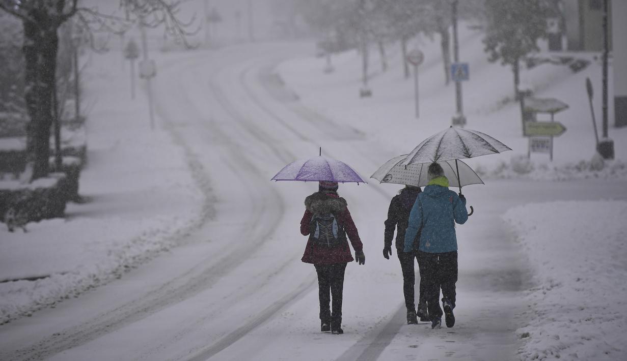 Orang-orang berjalan di bawah payung melalui lanskap bersalju, di El Espinal, Spanyol utara, Sabtu (27/11/2021). Pihak berwenang mengumumkan salju dan suhu rendah yang ekstrem selama beberapa hari ke depan di seluruh bagian utara negara itu. (AP Photo/Alvaro Barrientos)
