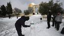 Seorang pria Palestina membuat patung salju berbentuk roket di sebelah Kubah Batu di kompleks Masjid Al Aqsa di Kota Tua Yerusalem, Kamis (27/1/2022). Hujan salju yang jarang melanda sebagian wilayah Israel dan Tepi Barat, menutup sekolah dan bisnis. (AP Photo/Mahmoud Illean)