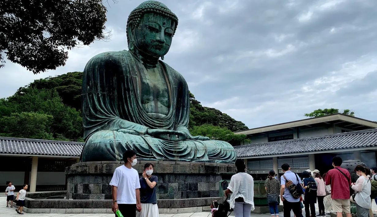 Orang-orang mengenakan masker saat mengunjungi The Great Buddha atau yang biasa disebut Kamakura Daibutsu di kuil Kotoku-in di Kamakura, Prefektur Kanagawa, Jepang, Sabtu (20/6/2020). Patung Buddha dari perunggu yang menjulang dengan tinggi 13,35 meter ini didirikan tahun 1252. (Behrouz MEHRI/AFP)