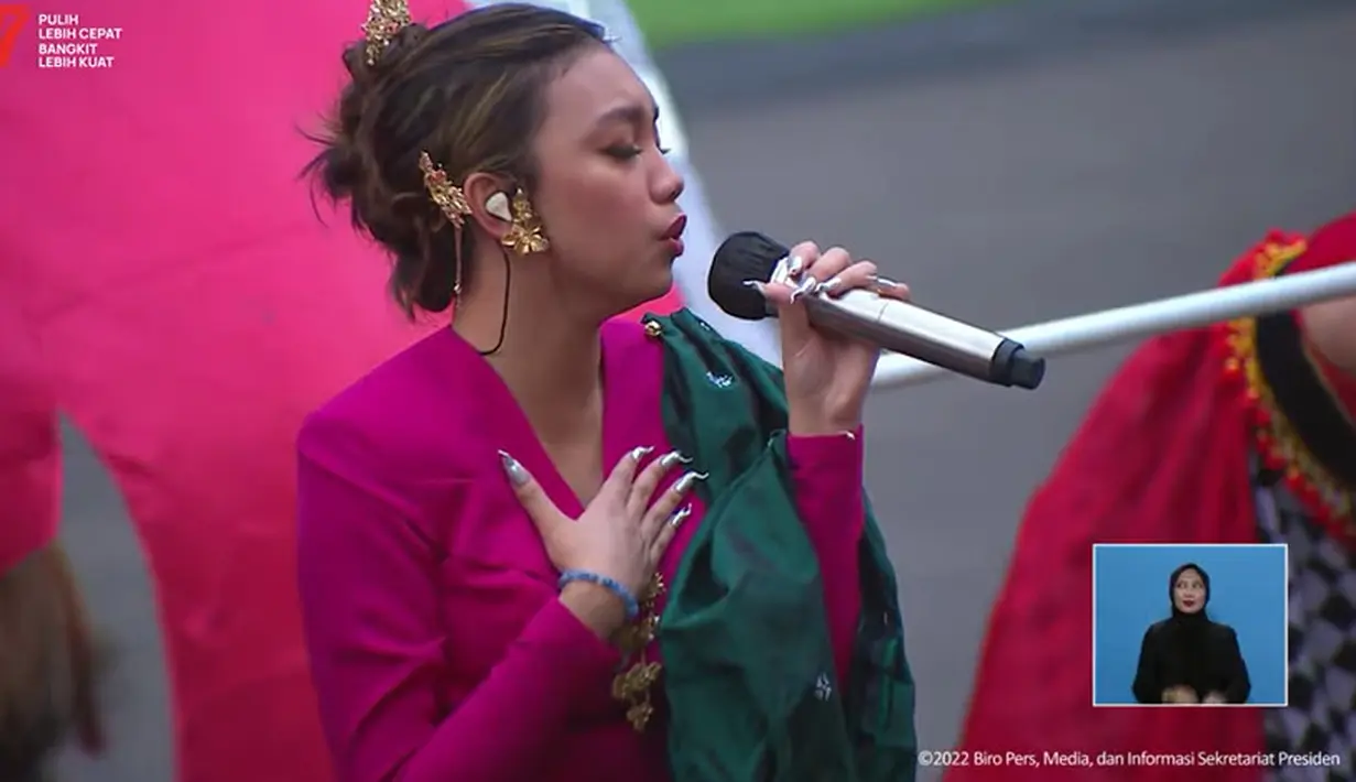 Mengenakan atasan lengan panjang berwarna pink fuschia yang dipadukan dengan kulot batik. Sebuah selendang yang berfungsi sebagai attachment di bahu kirinya berwarna hijau sehingga cukup kontras. (Tangkapan layar YouTube sekretariat Presiden)