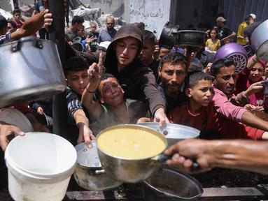 Para pengungsi Palestina berkumpul untuk mengambil makanan yang sudah dimasak dalam sebuah pembagian makanan di Jabalia, Jalur Gaza utara, pada 19 Mei 2025. (Bashar TALEB/AFP)