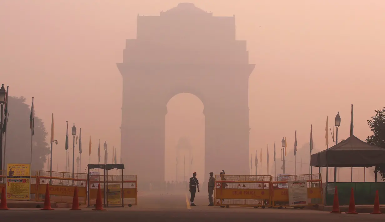 Petugas keamanan berjaga di depan India Gate yang diselimuti kabut tebal di New Delhi, India (31/10). Kabut tebal polusi ini menimbulkan kekhawatiran resiko berbagai penyakit yang berdampak pada penduduk kota New Delhi. (Reuters/Adnan Abidi)