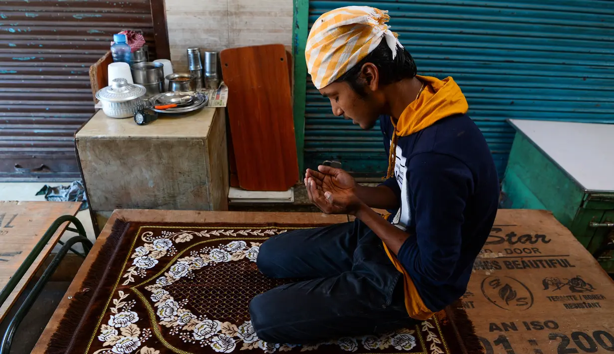 Umat Muslim melaksanakan salat di depan toko-toko yang tutup di sebuah pasar selama bulan Ramadan saat penerapan lockdown di New Delhi, Senin (4/5/2020). Di emperan toko-toko yang tutup, umat muslim salat berjemaah dengan menjaga jarak dan lainnya membaca kitab suci Alquran. (Sajjad HUSSAIN/AFP)