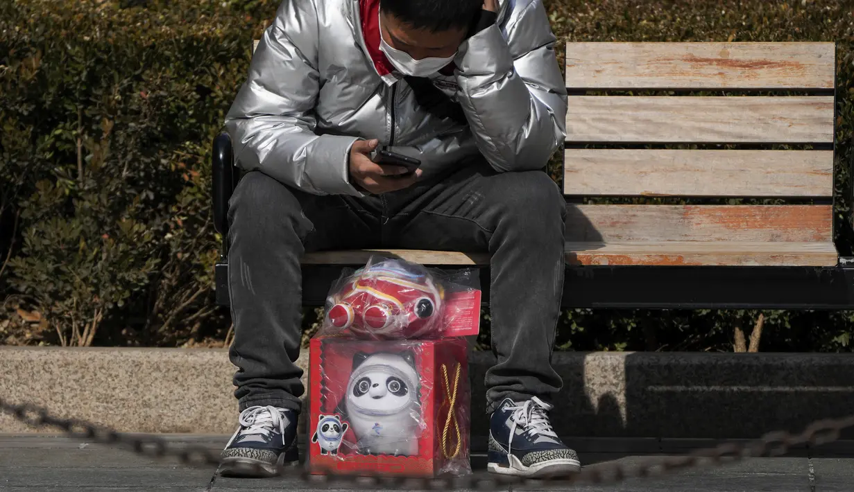 Seorang pria melihat-lihat ponsel saat beristirahat di bangku dengan boneka maskot Olimpiade Bing Dwen Dwen yang dibeli dari toko yang menjual memorabilia resmi Olimpiade di Beijing, 21 Februari 2022. Boneka Bing Dwen Dwen masih tetap populer meskipun Olimpiade telah berakhir. (AP Photo/Andy Wong)