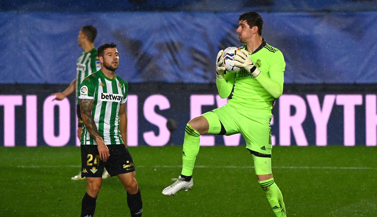 Kiper Real Madrid, Thibaut Courtois (kanan) menangkap bola dari ancaman striker Real Betis, Aitor Ruibal dalam laga lanjutan Liga Spanyol 2020/2021 pekan ke-33 di Alfredo Di Stefano Stadium, Madrid, Sabtu (24/4/2021). Real Madrid bermain imbang 0-0 dengan Real Betis. (AFP/Gabriel Bouys)