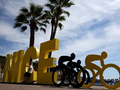 Wisatawan duduk di tulisan Nice dekat ornamen Tour de France2020 di kota Nice, French Riviera, Rabu (26/8/2020). Ajang balap sepeda lintas kota di Prancis ini akan dimulai dari kota Nice pada 29 Agustus hingga 20 September di bawah bayang-bayang ‘gelombang kedua’ COVID-19. (Kenzo Tribouillard/AFP)