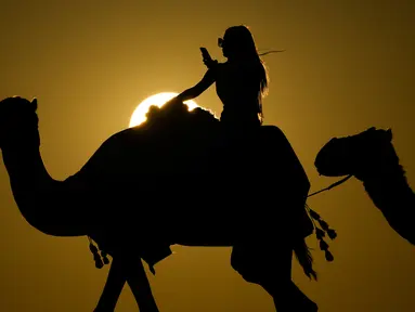 Seorang wanita melihat fotonya saat mengendarai unta di Mesaieed, Qatar, 26 November 2022. Kerumunan penggemar Piala Dunia di Qatar mencari sesuatu untuk dilakukan di antara pertandingan meninggalkan Doha untuk pengalaman wisata Teluk klasik: menunggang unta di gurun. Tetapi peningkatan turis yang tiba-tiba memberi tekanan pada hewan, yang hampir tidak punya waktu untuk beristirahat di antara setiap perjalanan. (AP Photo/Ashley Landis)