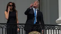 Presiden AS Donald Trump ditemani Ibu Negara, Melania Trump menunjuk ke atas saat menyaksikan  gerhana matahari dari balkon Gedung Putih di Washington, Senin (21/8). Trump tampak menatap langsung ke arah matahari dengan mata telanjang. (NICHOLAS KAMM/AFP)