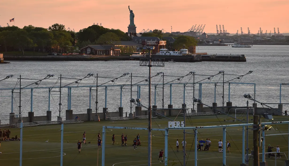 Para pemain bertanding sepak bola selama matahari terbenam di Brooklyn Bridge Park, New York City, Amerika Serikat, 20 Mei 2018. Olahraga semakin berkesan dengan latar belakang Patung Liberty. (HECTOR RETAMAL/AFP)