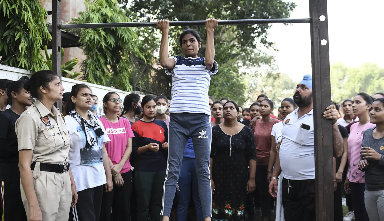 Petugas Polisi Punjab menyaksikan seorang wanita muda melakukan pull-up selama sesi pelatihan untuk bergabung dengan Polisi Punjab di Amritsar, India, Senin (28/6/ 2021). (AFP/Narider Nanu)