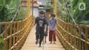 Anak-anak melintasi jembatan gantung Kuning yang menghubungkan Pasar Minggu Poltangan ke Cililitan Condet, Jakarta, Selasa (28/12/2021). Jembatan gantung Kuning dengan panjang 40 meter di atas sungai Ciliwung tersebut baru baru ini dijadikan lokasi foto untuk konten medsos. (merdeka.com/Imam Buhori)