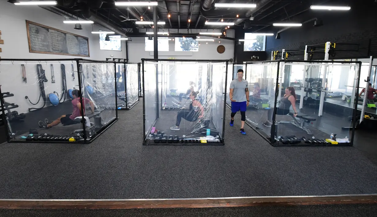 Peet Sapsin memimpin kelas dengan orang-orang berada dalam kotak plastik di Inspire South Bay Fitness di Redondo Beach, California pada 15 Juni 2020. Ruangan gym dengan plastik sebagai pemisah itu agar pengunjung dapat tetap berolahraga sambil tetap menjaga jarak fisik. (FREDERIC J. BROWN / AFP)