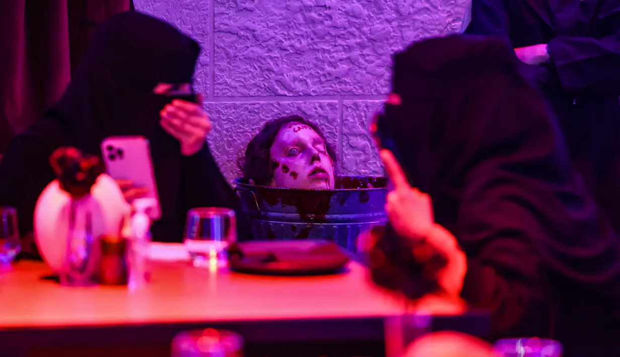 Pengunjung tertawa ketika penyangga kepala zombie ditempatkan di dekat meja mereka di restoran "Shadows" bertema horor di Riyadh, Arab Saudi, 19 Januari 2022. Restoran tersebut menawarkan pelanggan hidangan dengan tengkorak dan darah ditemani zombie serta vampir (Fayez Nureldine/AFP)