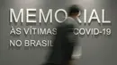 Seorang pria melewati dinding yang bertuliskan dalam bahasa Portugis "Memorial untuk para korban COVID-19 di Brasil," di gedung Senat Brasil di Brasilia, 15 Februari 2022. Monumen tersebut terdiri dari 27 prisma, mewakili negara bagian Brasil. (AP/Claudio Reis)