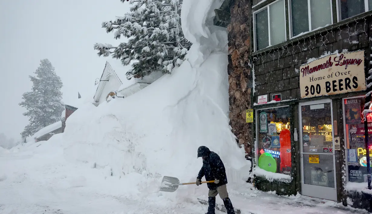Sekop Spike Todd di depan tokonya dekat gundukan salju yang menumpuk dari badai sebelumnya selama badai musim dingin di pegunungan Sierra Nevada di Danau Mammoth, California pada 10 Maret 2023. Todd berkata, 'Saya telah tinggal di sini selama 43 tahun dan ini akan menjadi musim dingin terbesar yang pernah saya lihat.' (Mario Tama/Getty Images/AFP)